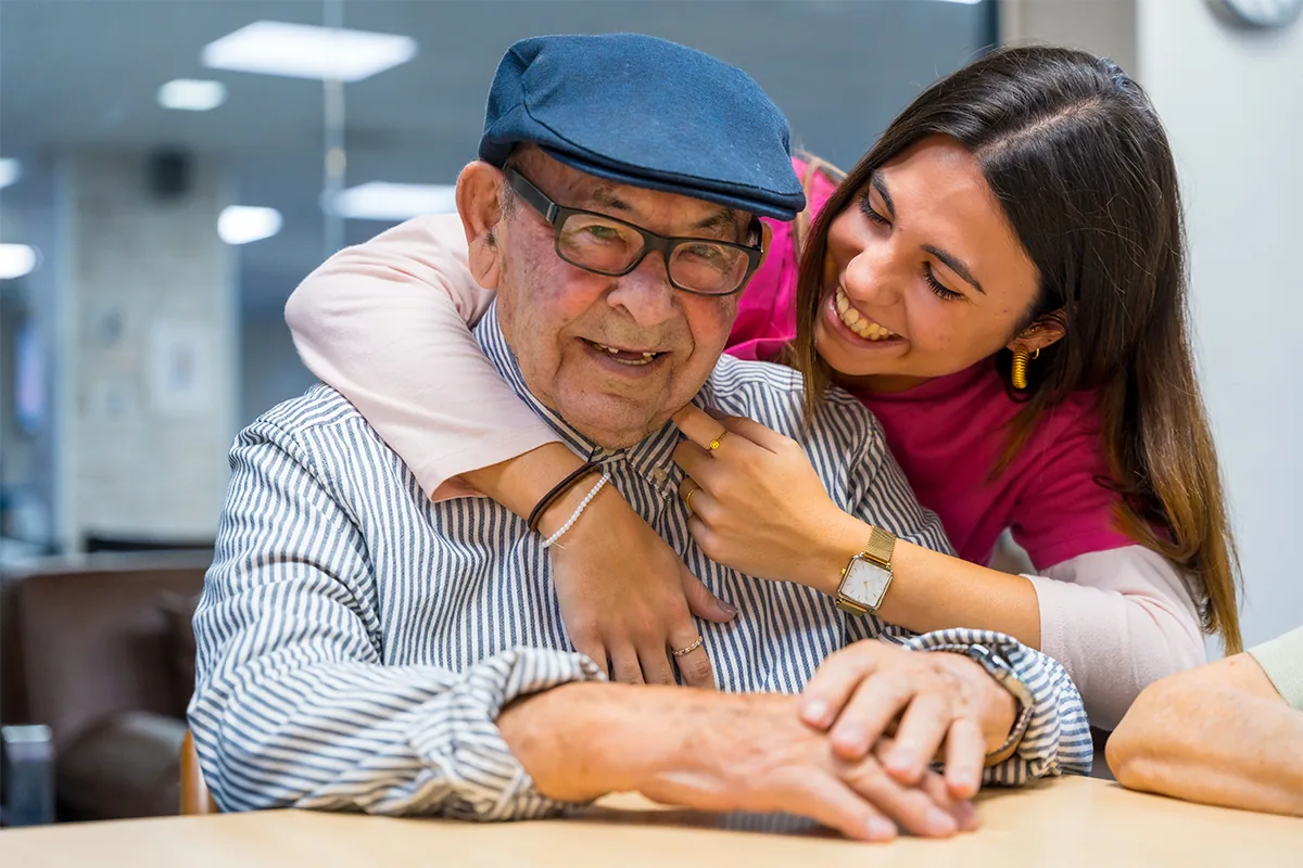 An older man smiling while being embraced by a younger woman